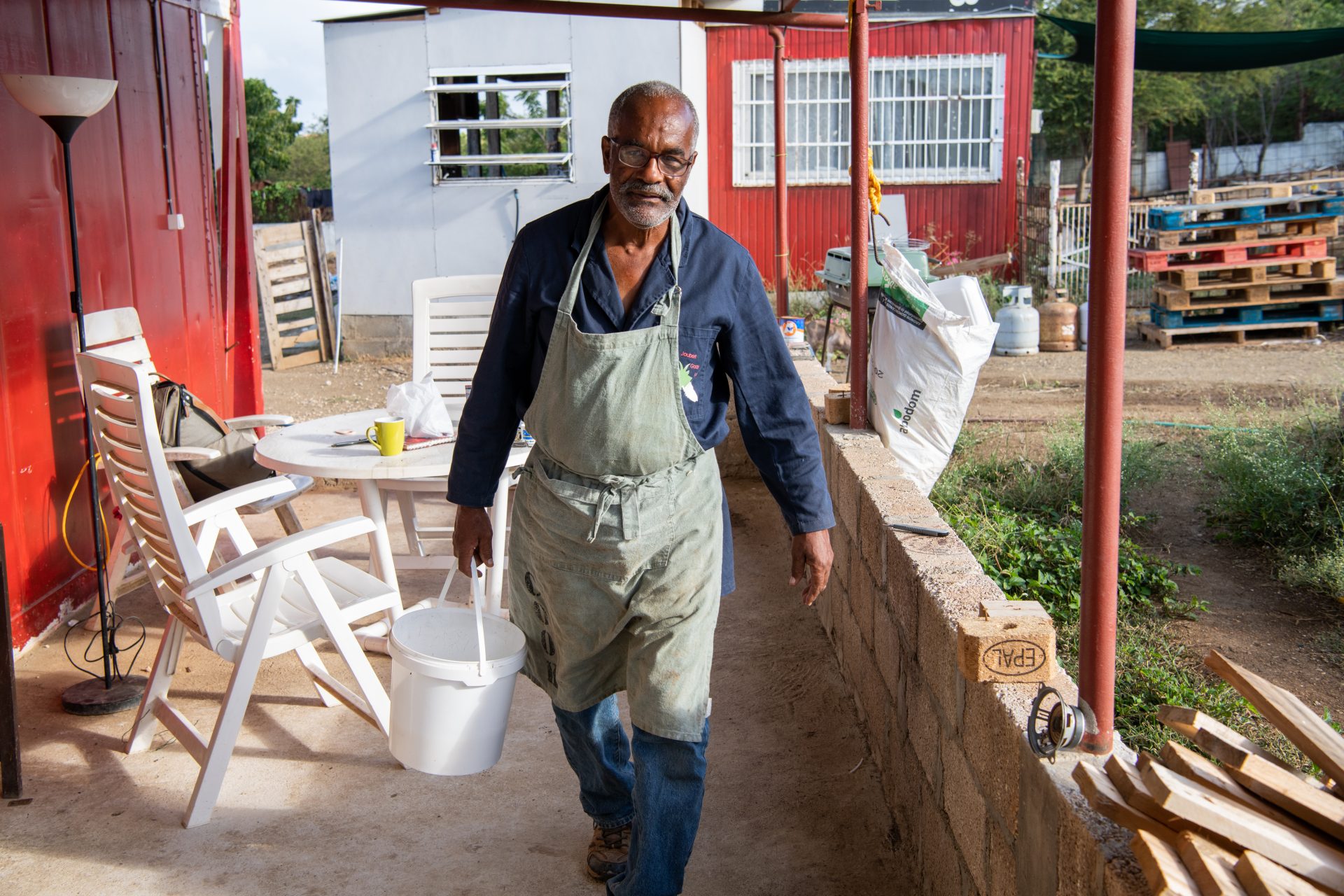 Older man is walking around a farm holding a white bucket